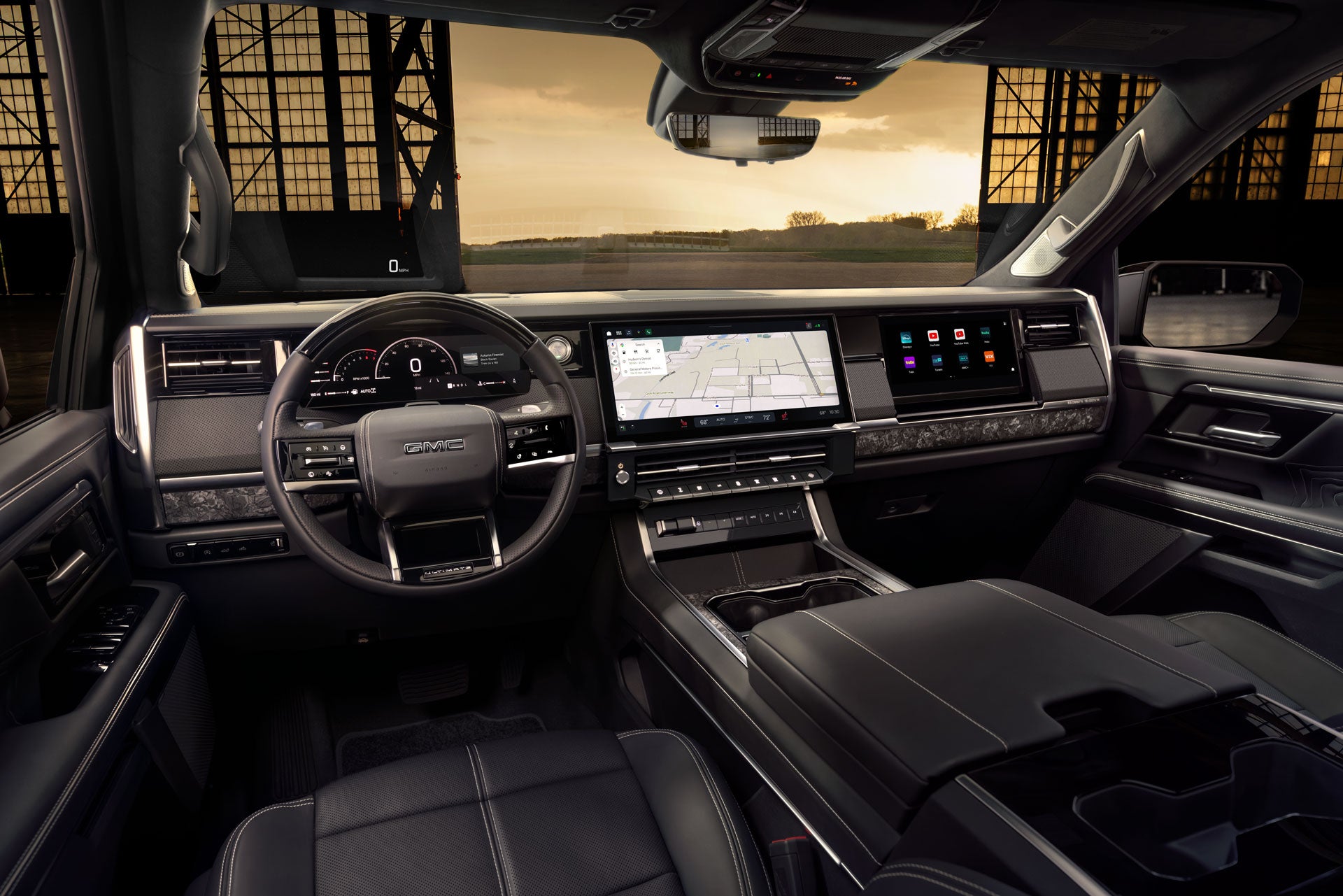 A GMC steering wheel with a digital display showing 0 mph, rpm, fuel, temperature, and current song.